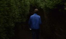 A man in a blue coat inside a hedge