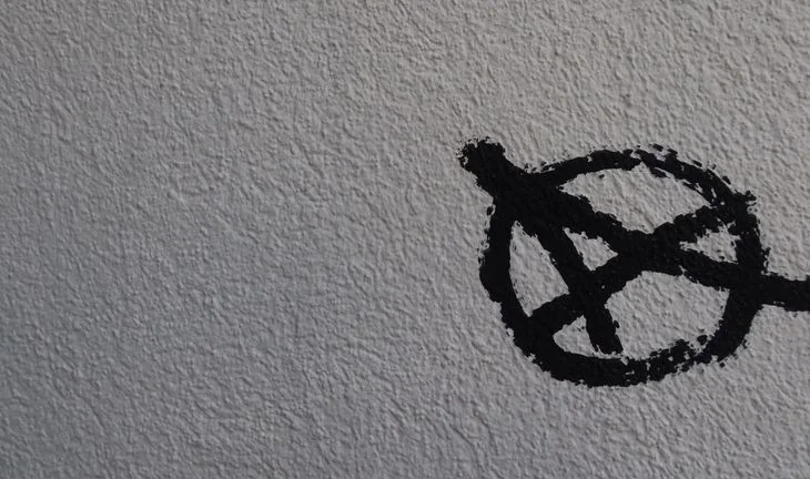 A black anarchy sign on a stibbly white wall 